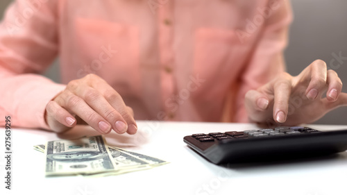 Female calculating monthly expenses, dollar banknotes on table, taxes payment