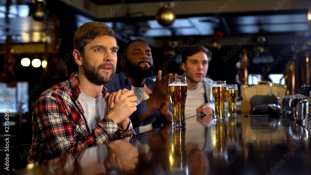 Anxious multiracial friends cheering for sports game in pub, watching game on tv