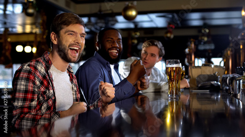 Multiracial male friends celebrating victory, cheering for favorite team in bar