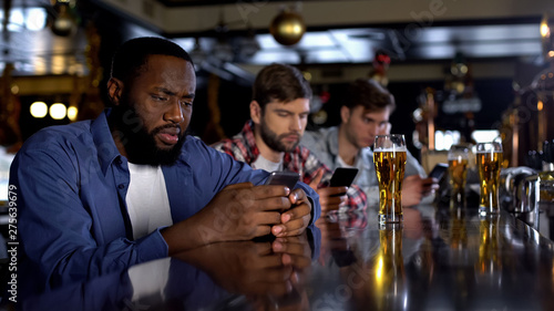 Bored men scrolling phones in pub replacing live communication, gadget addiction