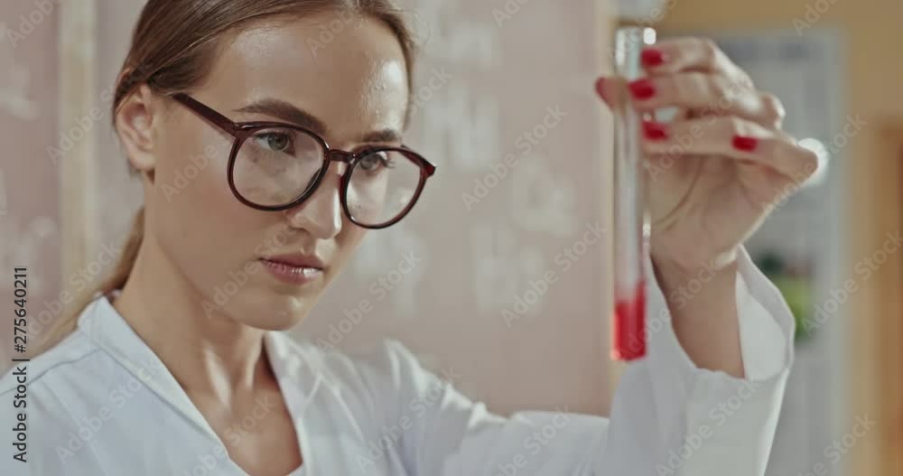 Young female chemist doing tests or experiments in a laboratory checking a chemical mixture in a test tube for a color change or reaction. Medium close up. Young female chemist doing tests or experiments in a laboratory checking a chemical mixture in a test tube for a color change or reaction. Medium close up.