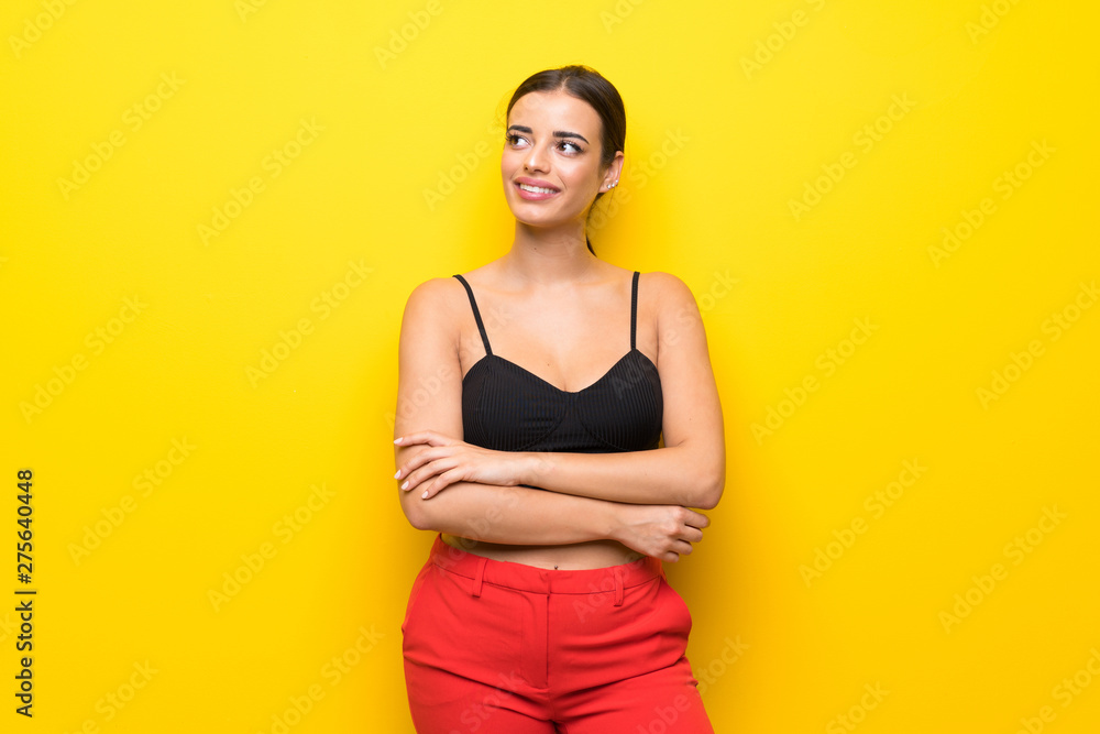 Obraz premium Young woman over isolated yellow background looking up while smiling