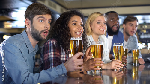 Sport fans holding beer glasses attentively watching sport competition in pub