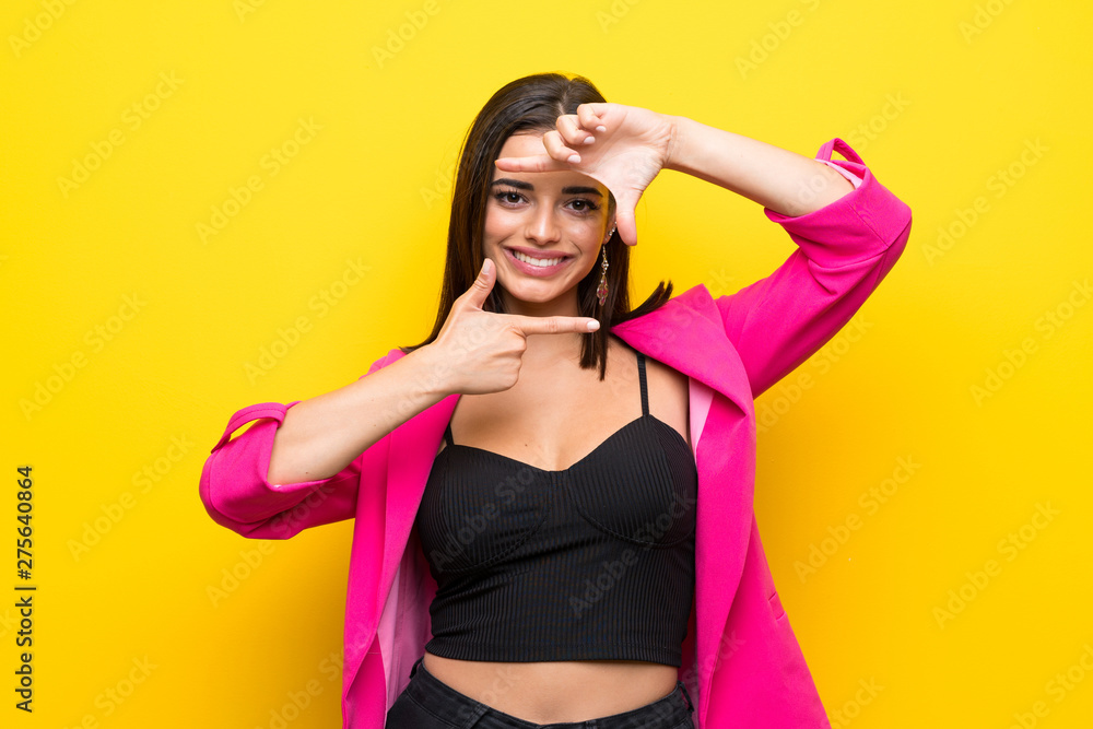 Young woman over isolated yellow background focusing face. Framing symbol Young woman over isolated yellow background focusing face. Framing symbol