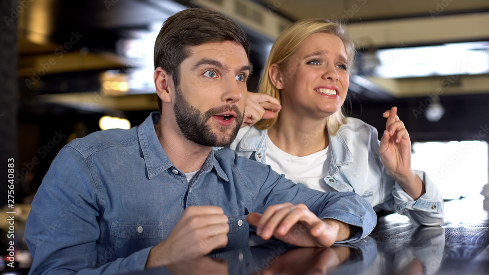 Nervous couple watching competition in bar, supporting their favorites, fun Nervous couple watching competition in bar, supporting their favorites, fun