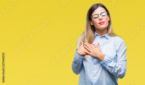 Young beautiful business woman wearing glasses over isolated background smiling with hands on chest with closed eyes and grateful gesture on face. Health concept. © Krakenimages.com
