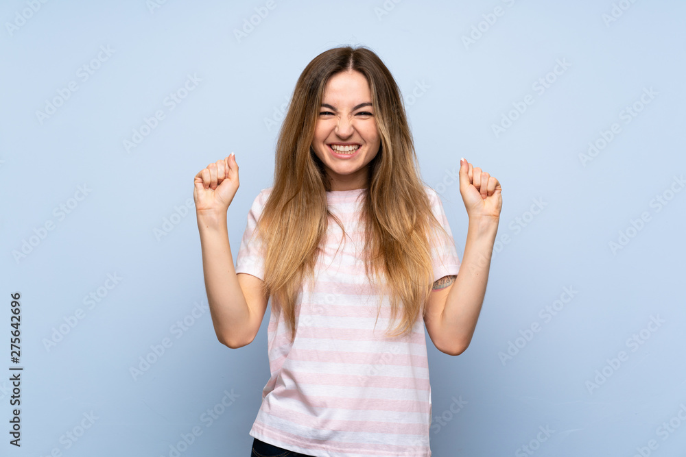 Fototapeta premium Young woman over isolated blue background celebrating a victory in winner position