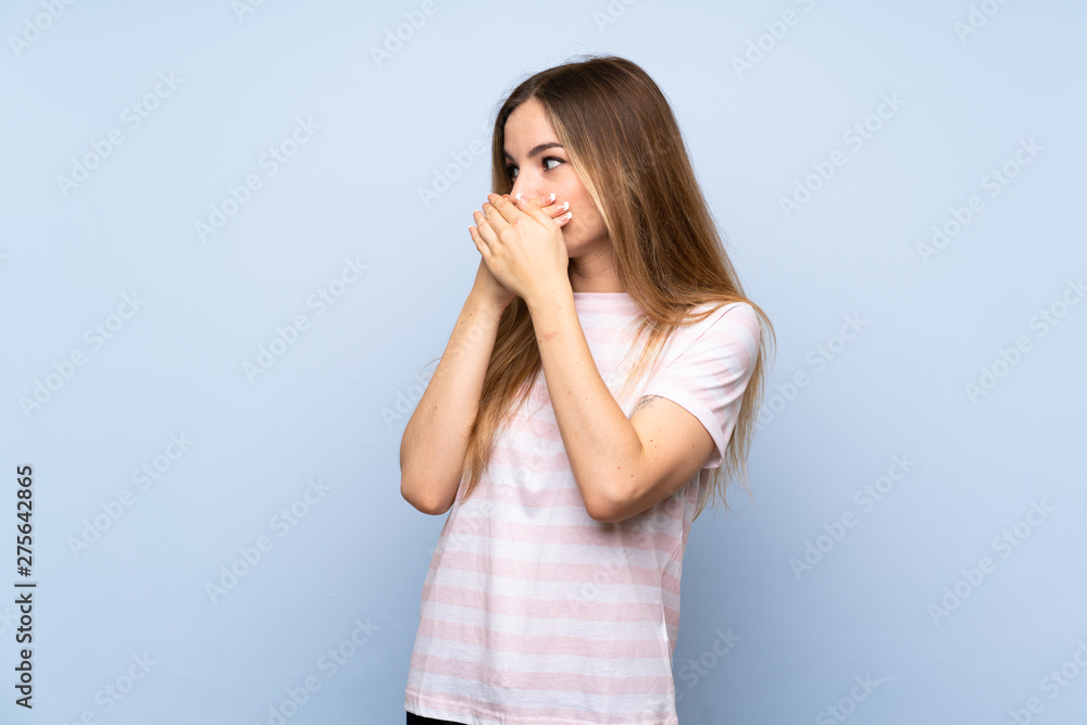 Young woman over isolated blue background covering mouth and looking to the side Young woman over isolated blue background covering mouth and looking to the side