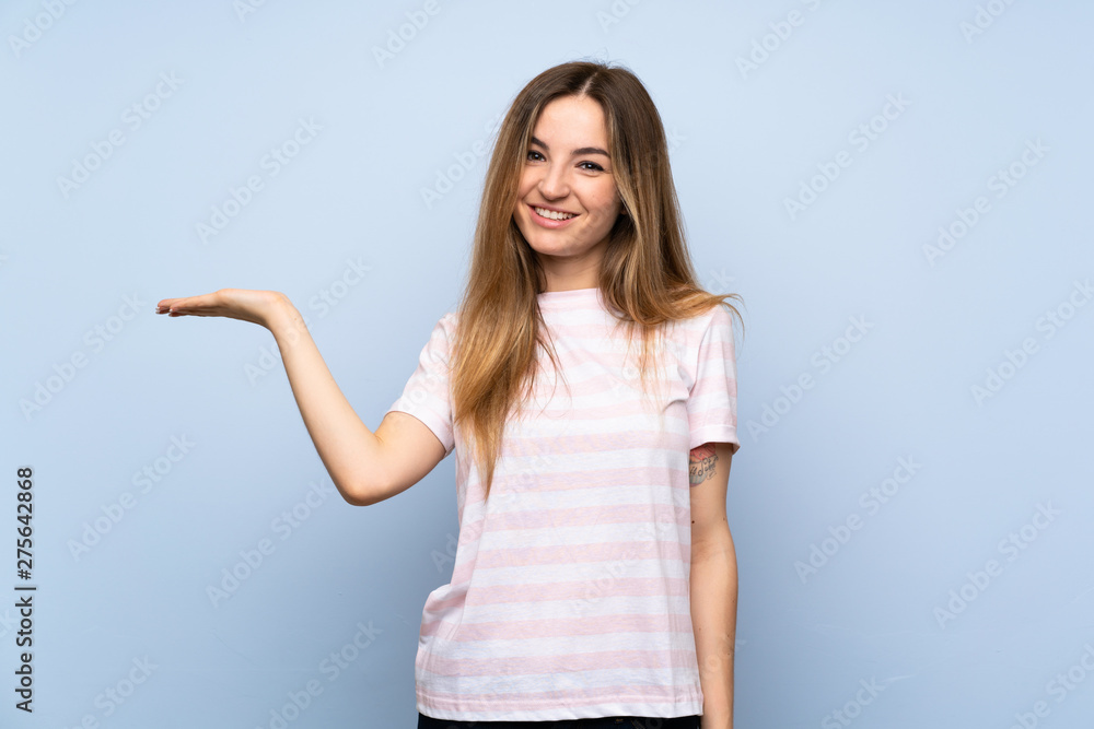 Young woman over isolated blue background holding copyspace imaginary on the palm to insert an ad Young woman over isolated blue background holding copyspace imaginary on the palm to insert an ad