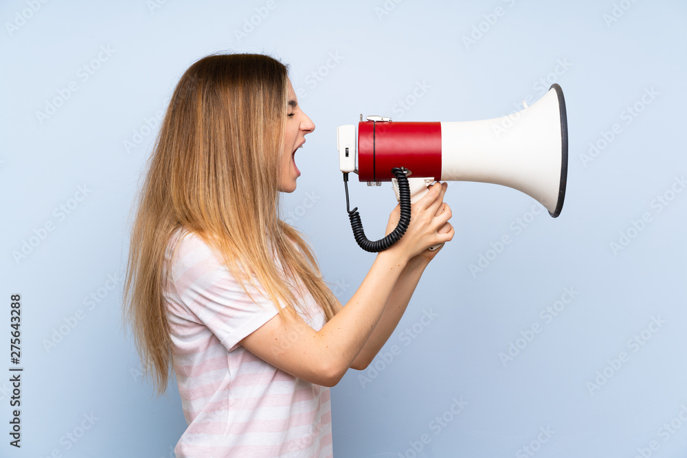 Young woman over isolated blue background shouting through a megaphone Young woman over isolated blue background shouting through a megaphone