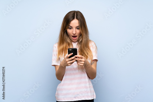 Young woman over isolated blue background surprised and sending a message
