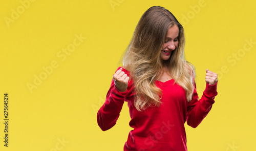 Young beautiful blonde woman wearing red sweater over isolated background very happy and excited doing winner gesture with arms raised, smiling and screaming for success. Celebration concept.