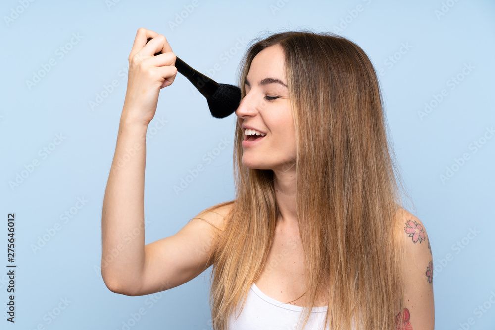 Young woman over isolated blue background with makeup brush Young woman over isolated blue background with makeup brush