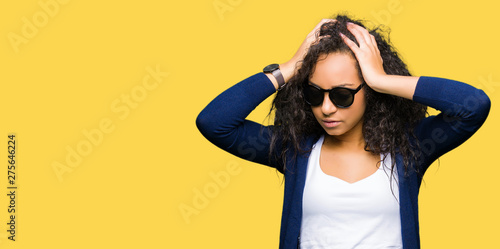 Young beautiful girl with curly hair wearing fashion sunglasses suffering from headache desperate and stressed because pain and migraine. Hands on head.