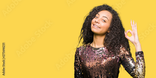 Young beautiful girl with curly hair wearing night party dress smiling positive doing ok sign with hand and fingers. Successful expression.