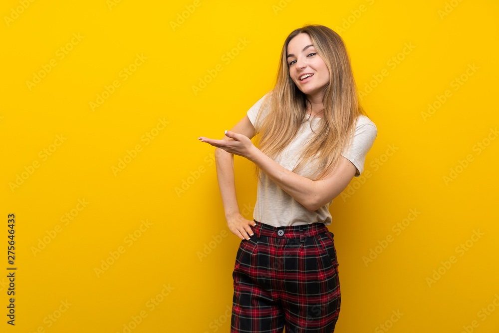 Young woman over isolated yellow wall extending hands to the side for inviting to come Young woman over isolated yellow wall extending hands to the side for inviting to come