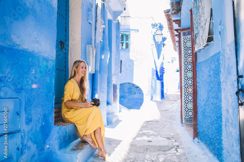 Positive woman using retro equipment while resting near blue building of Chaouen enjoying summer trip for visit ancient city, cheerful Caucasian tourist with vintage camera recreating outdoors © BullRun