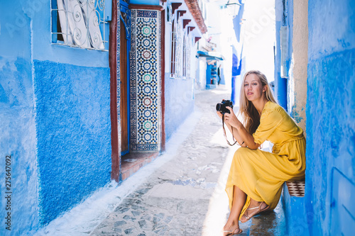 Portrait of attractive skilled female amateur photographer with retro technology taking rest on urban setting of Chaouen city, beautiful woman with vintage equipment looking at camera on leisure © BullRun