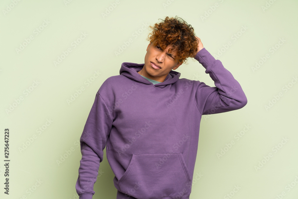 Young african american man over isolated green wall having doubts while scratching head Young african american man over isolated green wall having doubts while scratching head