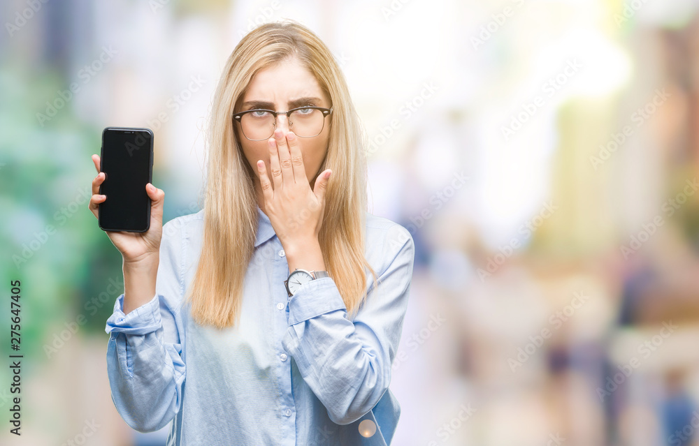 Young beautiful blonde business woman showing screen of smartphone over isolated background cover mouth with hand shocked with shame for mistake, expression of fear, scared in silence, secret concept