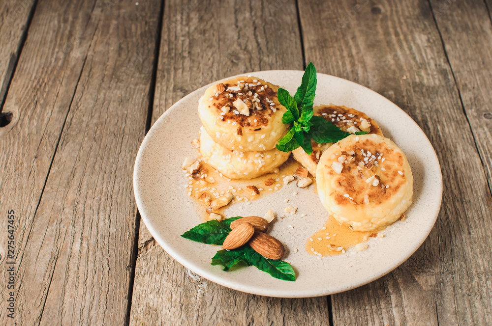 Delicious breakfast - cottage cheese pancakes, cheesecakes, cottage cheese pancakes with almonds, mint and maple syrup in a beige plate. Useful dessert on a wooden table in rustic style. Selective foc