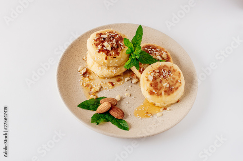 Delicious breakfast - cottage cheese pancakes, cheesecakes, cottage cheese pancakes with almonds, mint and maple syrup in a beige plate. Useful dessert on white background (isolate)