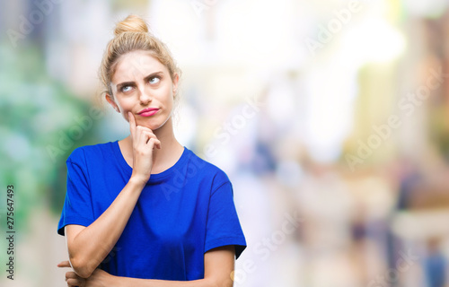 Young beautiful blonde and blue eyes woman wearing blue t-shirt over isolated background with hand on chin thinking about question, pensive expression. Smiling with thoughtful face. Doubt concept.