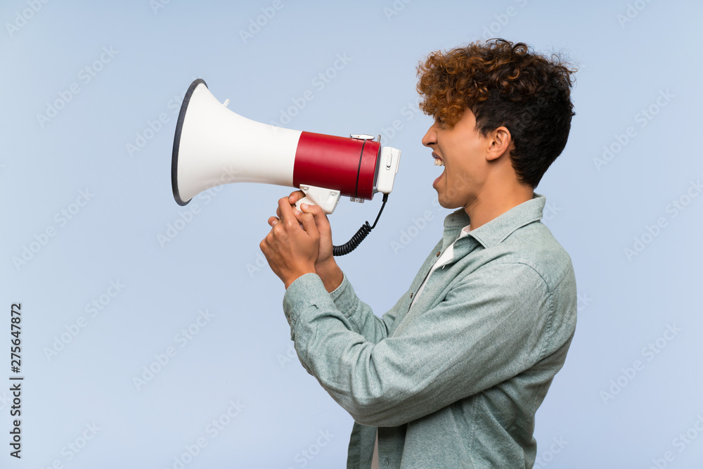 Young african american man over isolated blue wall shouting through a megaphone Young african american man over isolated blue wall shouting through a megaphone