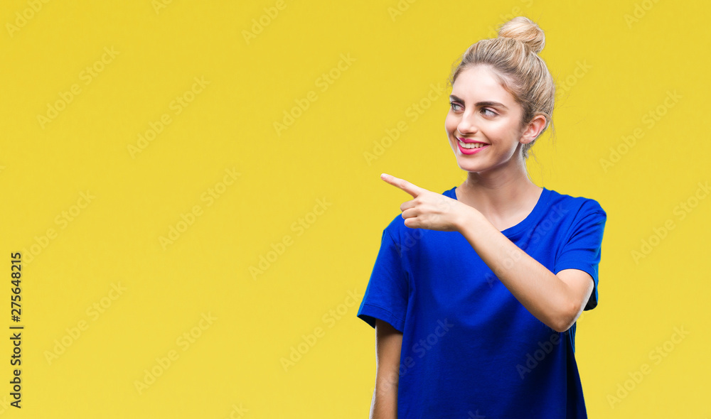 Young beautiful blonde and blue eyes woman wearing blue t-shirt over isolated background cheerful with a smile of face pointing with hand and finger up to the side with happy and natural expression Young beautiful blonde and blue eyes woman wearing blue t-shirt over isolated background cheerful with a smile of face pointing with hand and finger up to the side with happy and natural expression