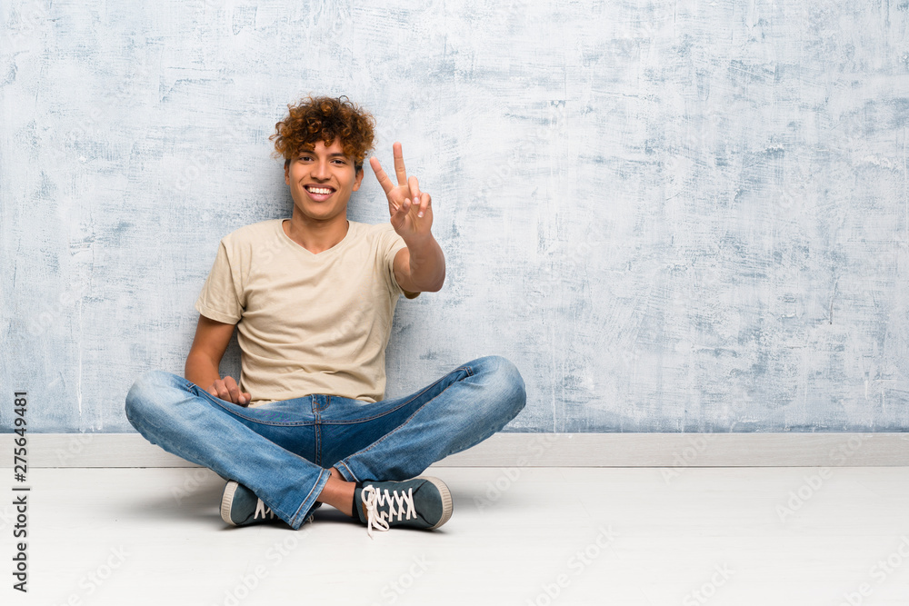 Young african american man sitting on the floor smiling and showing victory sign