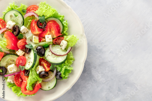 Greek salad. A closeup photo of a plate of fresh salad with lettuce, feta cheese, tomatoes, cucumbers, onions and olives, shot from the top with copy space