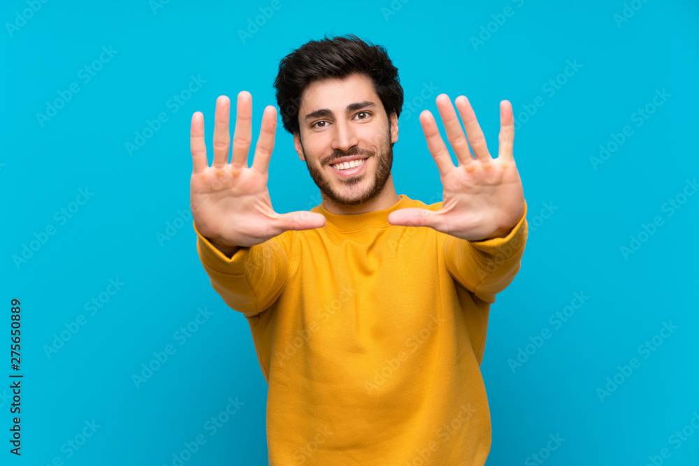 Handsome over isolated blue wall counting ten with fingers Handsome over isolated blue wall counting ten with fingers