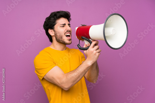 Handsome over isolated purple wall shouting through a megaphone