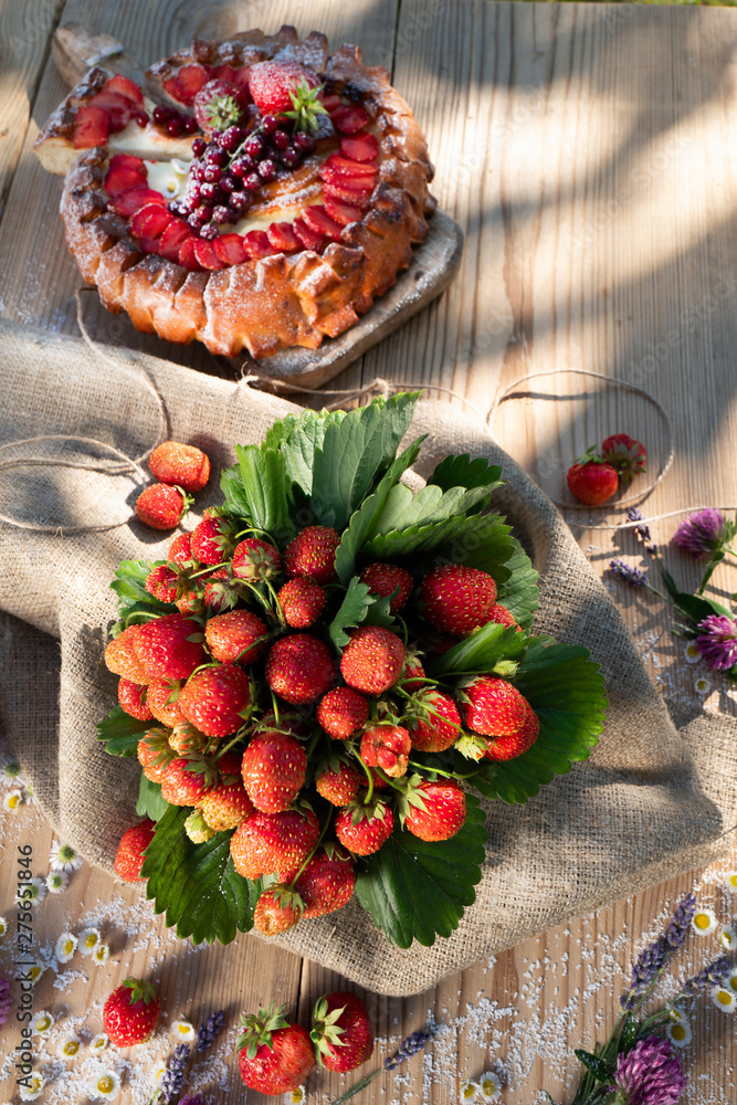 Fresh strawberries from the garden bed on the table with pie and flowers