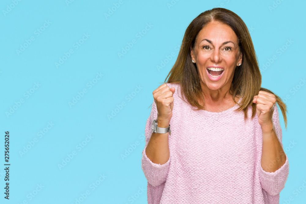 Fototapeta premium Beautiful middle age adult woman wearing winter sweater over isolated background celebrating surprised and amazed for success with arms raised and open eyes. Winner concept.