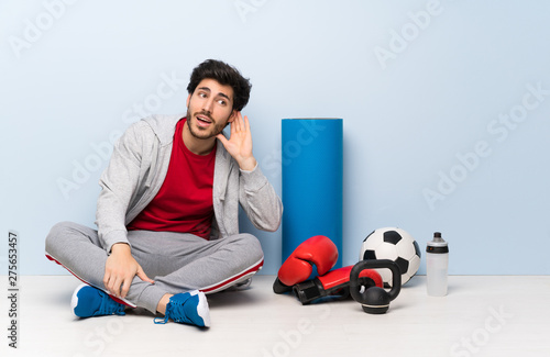 Sport man sitting on the floor listening to something by putting hand on the ear