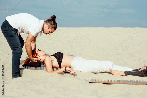 extreme yoga training - relaxation and self-development - man trainer  master  helping beautiful office woman to lay with nacked back on the board with nails in desert outdoor