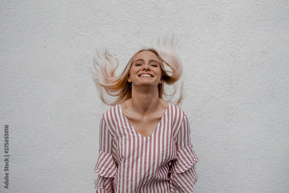 Wind in hair. Happy beautiful european woman having expressive emotions, laughing and dancing outdoors over white street wall background. Curly hair, trendy fashion wear. Modern and positive teenager Wind in hair. Happy beautiful european woman having expressive emotions, laughing and dancing outdoors over white street wall background. Curly hair, trendy fashion wear. Modern and positive teenager