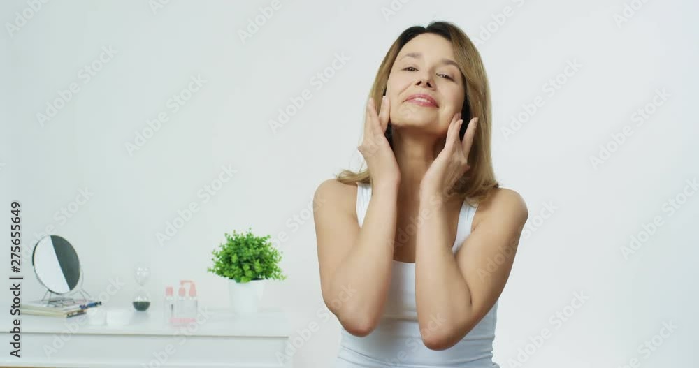 Portrait shot of the pretty young cheerful woman touching her face and caressing her skin during morning beaty care routine. Portrait shot of the pretty young cheerful woman touching her face and caressing her skin during morning beaty care routine.