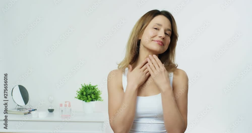Portrait shot of the Caucasian young attractive woman model massaging her neck during morning skin take care on the white wall background. Portrait shot of the Caucasian young attractive woman model massaging her neck during morning skin take care on the white wall background.