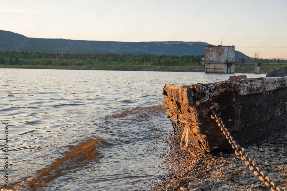 Old fishing boat on the lake at sunset tied with a chain. Old wooden boat on the shore