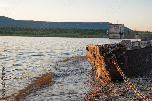 Old fishing boat on the lake at sunset tied with a chain. Old wooden boat on the shore