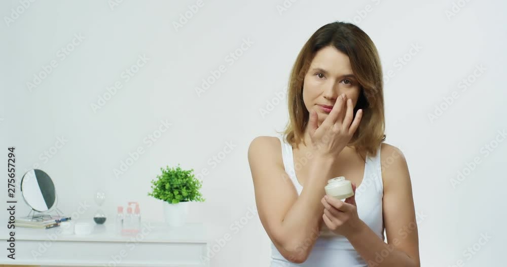 Good looking young Caucasian woman with perfect smooth skin applies white cream on her face and moisturizing it. Good looking young Caucasian woman with perfect smooth skin applies white cream on her face and moisturizing it.