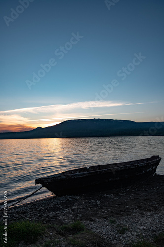 Old fishing boat on the lake at sunset tied with a chain. Old wooden boat on the shore © Eduard Vladimirovich
