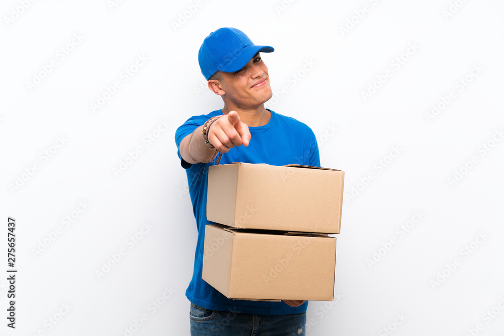 Delivery man over isolated white wall points finger at you with a confident expression Delivery man over isolated white wall points finger at you with a confident expression
