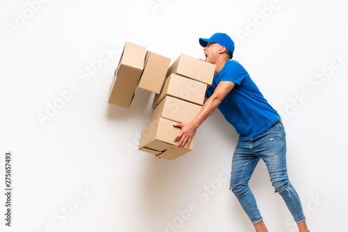 Delivery man over isolated white wall with lots boxes and stumbling