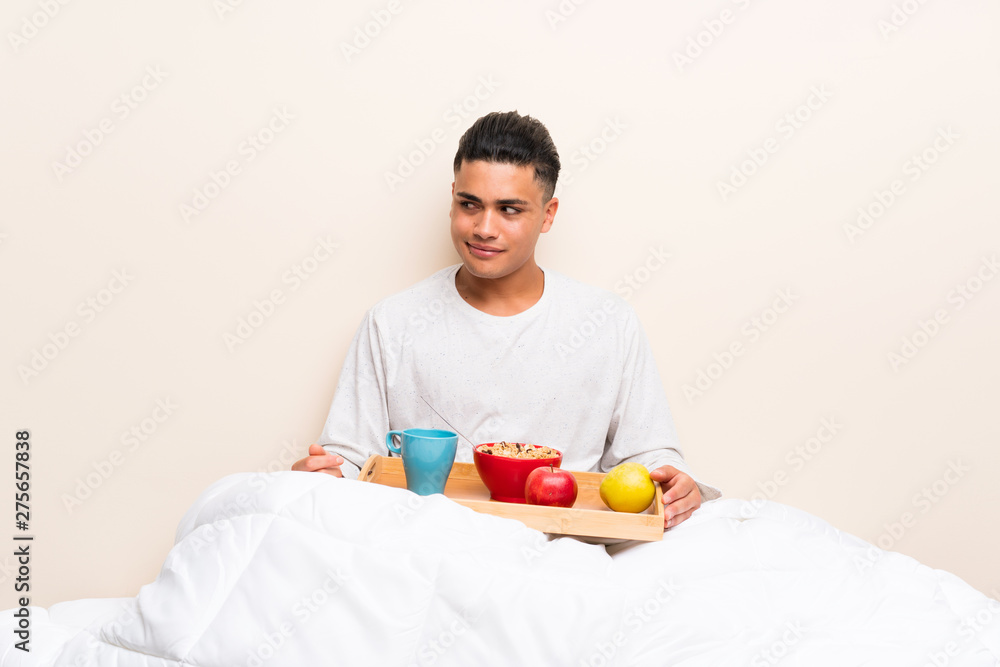 Young man having breakfast in bed standing and looking to the side Young man having breakfast in bed standing and looking to the side