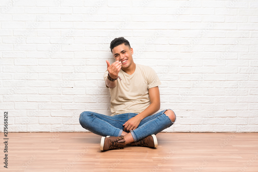 Young man sitting on the floor inviting to come Young man sitting on the floor inviting to come
