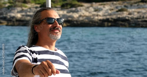 Handsone, happy man with long hair standing on a yacht deck and looking aroud. Relaxing under the sun at summer holiday. photo