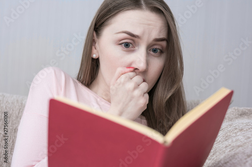 Scared girl sitting at home on the couch, reading a book, close up